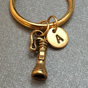 May include: Gold keychain with a small flashlight charm and a round charm with the letter A.