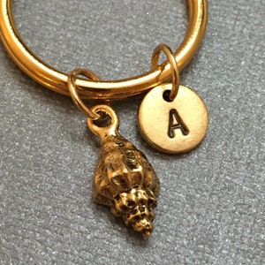 May include: Gold key ring with a seashell charm and a gold disc charm with the letter A.