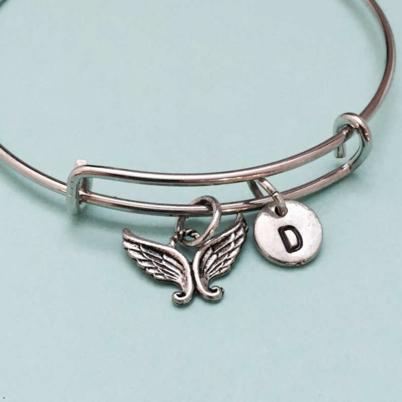 May include: A silver expandable bangle bracelet with a silver angel wing charm and a silver charm with the letter D.