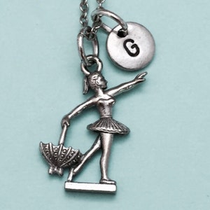 May include: Silver necklace with a ballerina charm holding an umbrella and a personalized initial charm with the letter "G".