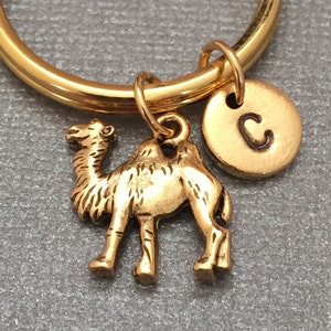 Op de afbeelding: Gouden sleutelhanger met een kameelbedel en een gouden schijfbedel met de letter C erop gegraveerd.
