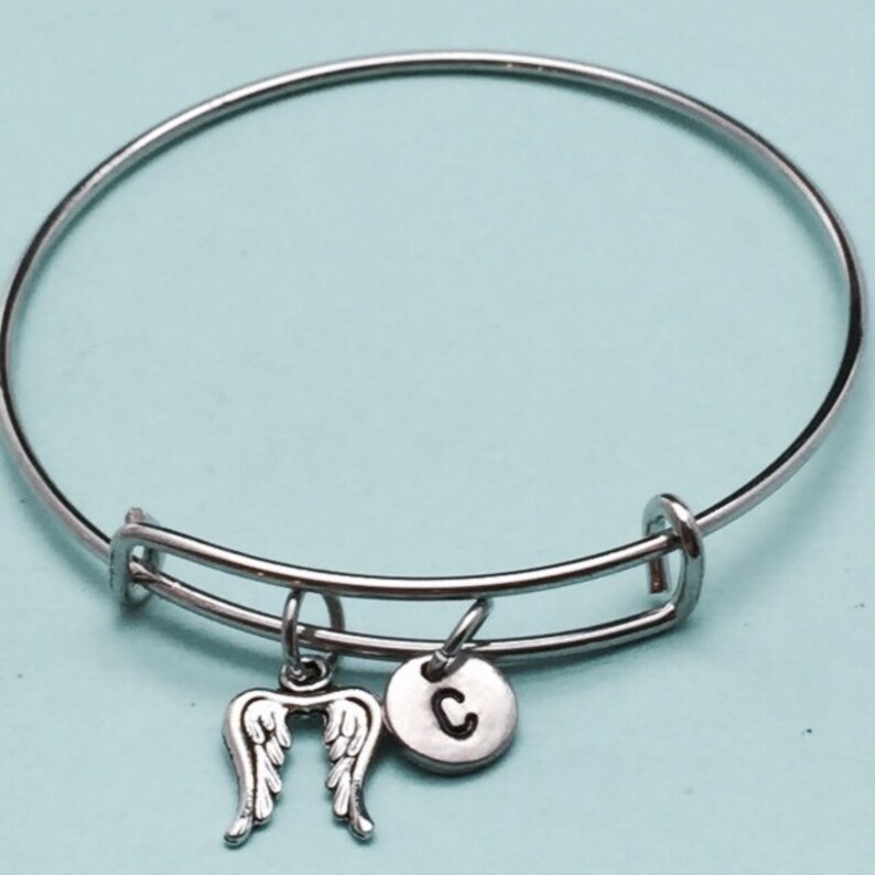 May include: A silver bangle bracelet with a charm of angel wings and a charm with the letter C.