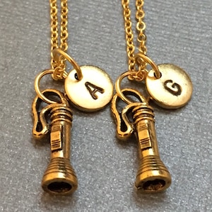 May include: Two gold necklaces with a flashlight charm and a round disc charm with the letters A and G on them.
