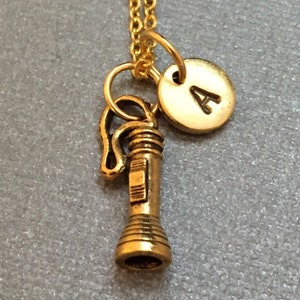 May include: Gold necklace with a flashlight charm and a gold initial charm with the letter A.
