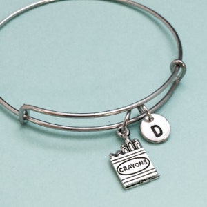 May include: Silver expandable bracelet with a charm of a box of crayons and a silver charm with the letter D.