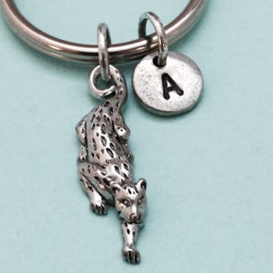 Puede incluir: Llavero de plata con un dije de leopardo detallado y un dije redondo con la letra 'A' grabada.