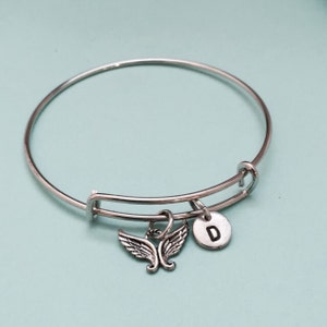 May include: Silver expandable bangle bracelet with a charm of angel wings and a silver disc with the letter D.