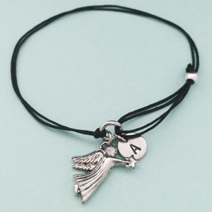 May include: A black cord bracelet with a silver angel charm and a silver charm with the letter A.