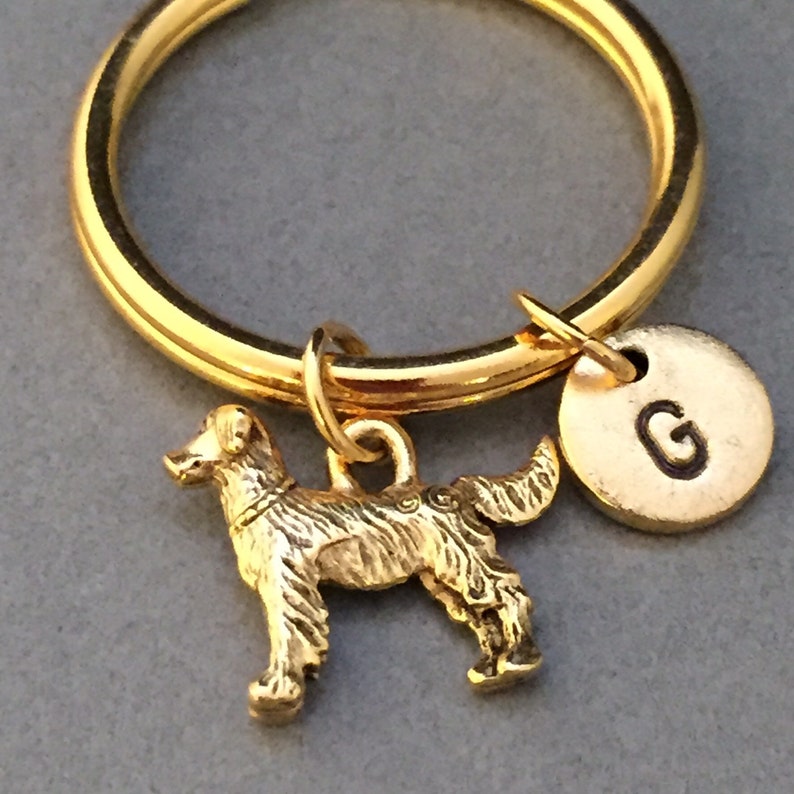 May include: Gold-toned keychain with a small golden dog charm and a round charm with the letter "G" engraved on it.