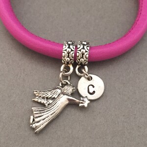 May include: A pink leather bracelet with two silver charms. One charm is a small angel with wings and the other is a round charm with the letter "C" engraved on it.