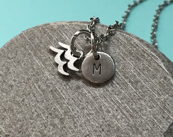 May include: Silver necklace with a charm that has the astrological symbol for Aquarius and a round charm with the letter M.
