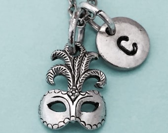 May include: Silver necklace with a masquerade mask charm and a letter 'C' charm.