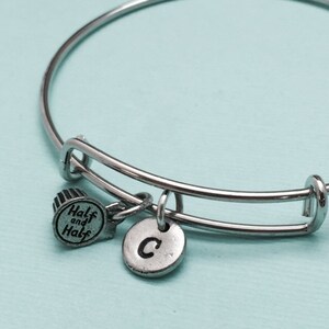 May include: A silver bangle bracelet with a charm that says "Half and Half" and a charm with the letter "C".