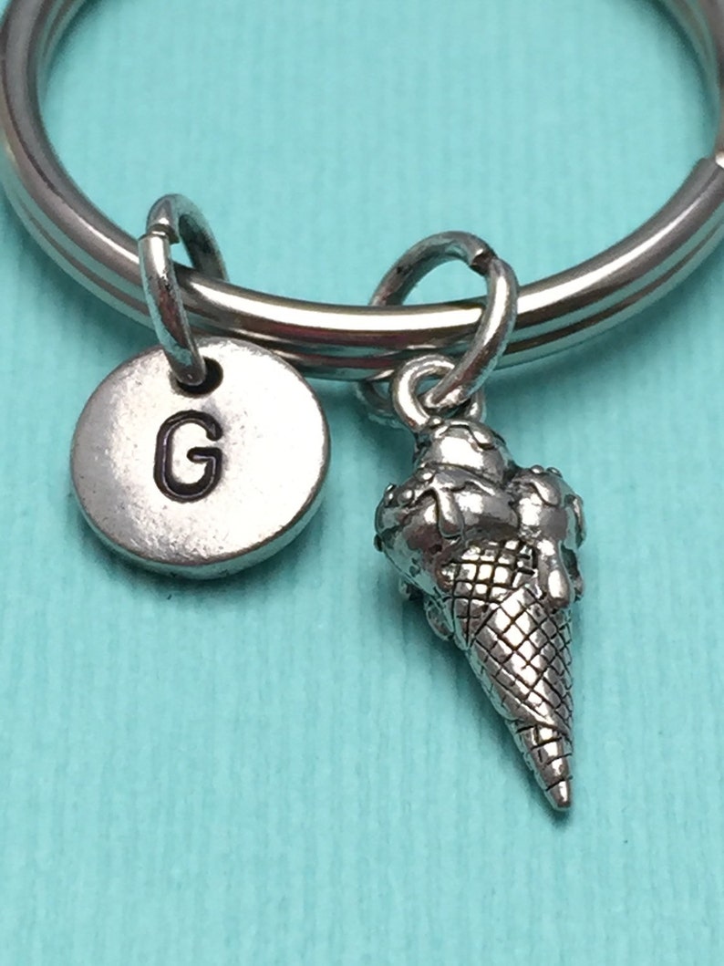 May include: Silver keychain with a letter G charm and a small ice cream cone charm. The keychain is on a turquoise background.