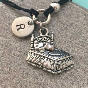 May include: A silver charm bracelet with a bed charm and a silver charm with the letter R. The bracelet is made of black cord.