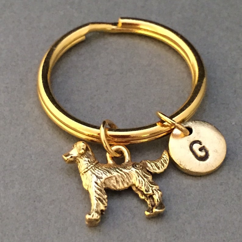 May include: Gold-toned keychain featuring a small golden dog charm and a round disc charm with the letter "G" engraved on it.