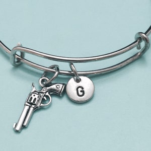 Op de afbeelding: Zilveren armband met een pistoolbedel en een letter G-bedel.