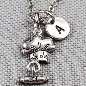 May include: Silver necklace with a chef hat charm, a rolling pin charm, and a letter A charm.