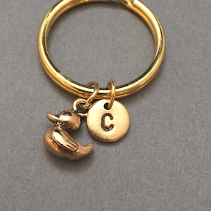 May include: Gold-toned keychain with a small gold-toned rubber duck charm and a round gold-toned charm with the letter 'C' engraved on it.