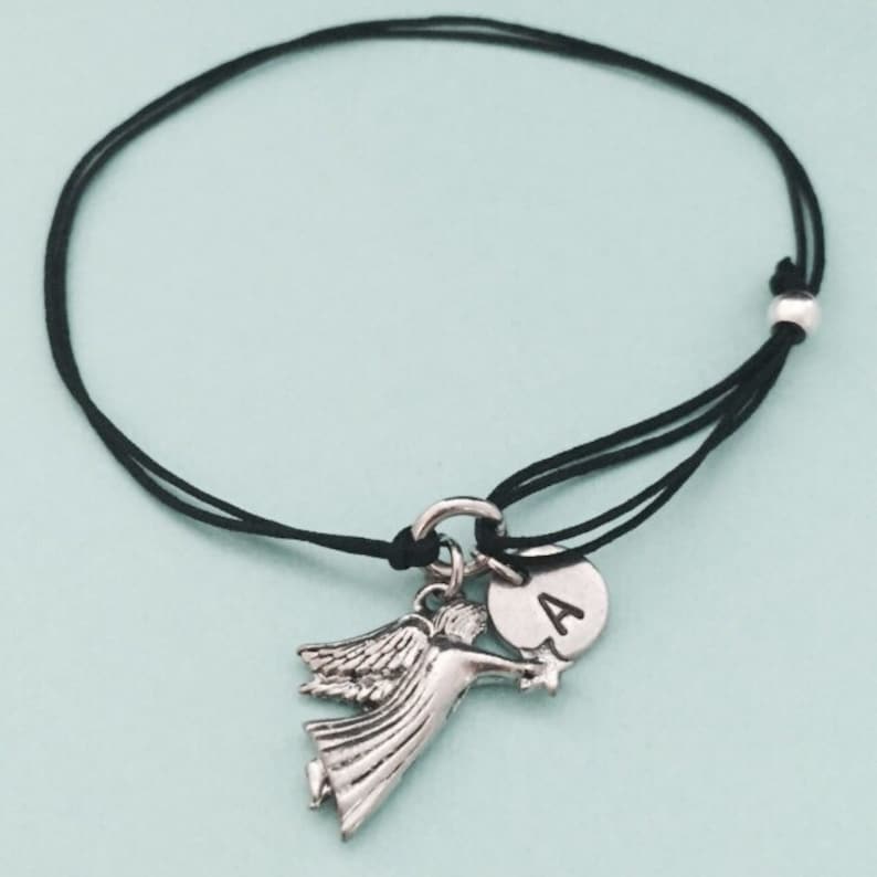 May include: A black cord bracelet with a silver angel charm and a silver charm with the letter A.