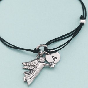 May include: A black string bracelet with a silver angel charm and a silver charm with the letter "A" on it.
