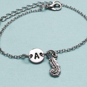 May include: A silver chain bracelet with a silver charm that has the letter 'A' on it and a feather charm.