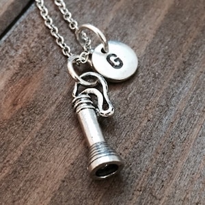 May include: Silver necklace with a small telescope charm and a round charm with the letter G.