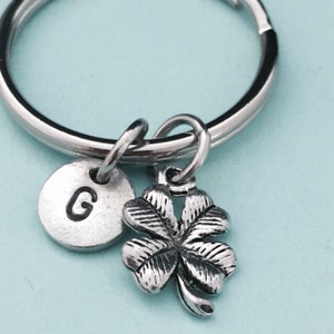 May include: Silver keychain with a four-leaf clover charm and a round charm with the letter G.