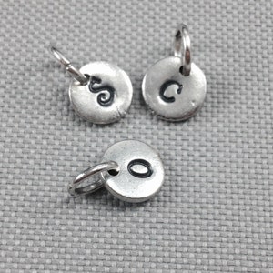May include: Three silver charms with a jump ring for attaching to a necklace or bracelet. Each charm has a letter stamped on it: S, C, and O.