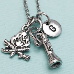 May include: Silver necklace with a charm of a campfire, a flashlight, and a letter G charm.