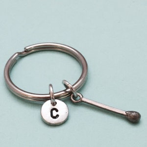 May include: Silver keychain with a letter C charm and a matchstick charm.