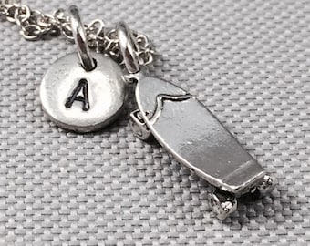 May include: Silver necklace with a skateboard charm and a round charm with the letter A.
