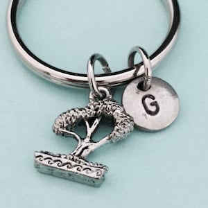 May include: Silver keychain with a small bonsai tree charm and a silver disc charm with the letter G.