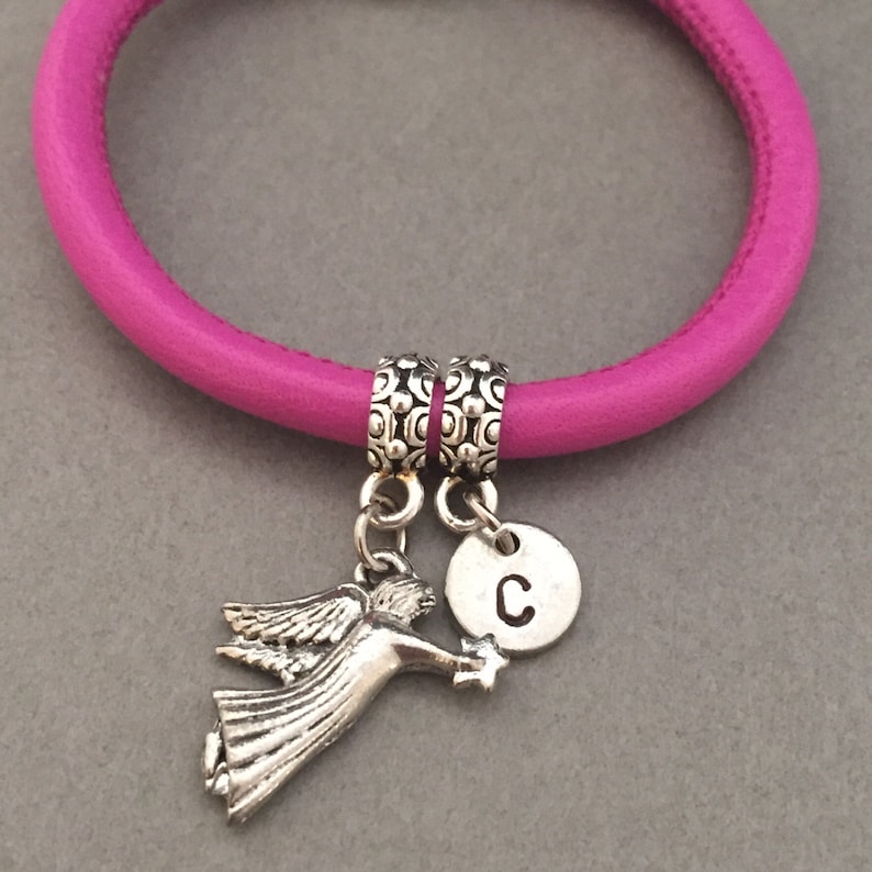 May include: A pink leather bracelet with two silver charm beads. One charm is a silver angel with a star and the other is a silver disc with the letter "C" engraved on it.