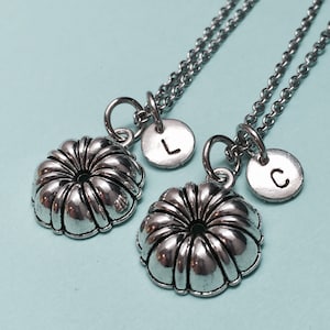 May include: Two silver necklaces with a small silver cake pan charm and a silver disc charm with the letter L on one necklace and the letter C on the other.