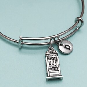 May include: A silver expandable bracelet with a charm of a silver London telephone booth and a silver charm with the letter "D" on it.