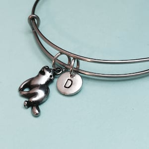 May include: A silver charm bracelet with a sloth charm and a silver charm with the letter D.