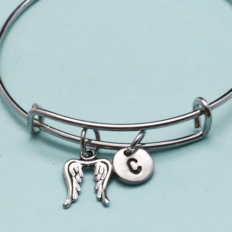 May include: A silver bangle bracelet with a charm of angel wings and a charm with the letter C.