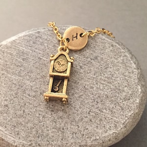 May include: Gold necklace with a small gold clock charm and a round gold charm with the letter "H" engraved on it.