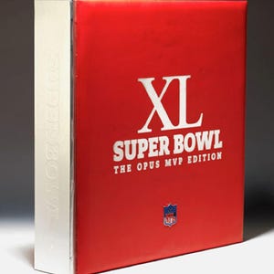 Op de afbeelding: Een rood boek met een zilveren rug. Het boek is getiteld "XL Super Bowl The Opus MVP Edition" en heeft het NFL-logo.