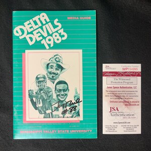 Può includere: Una guida multimediale verde e bianca per la squadra di football dei Delta Devils del 1983. La copertina presenta un cartone animato di un giocatore di football che indossa un casco e una maglia con il numero 88. La guida include un autografo firmato da James Spence Authentication, LLC.