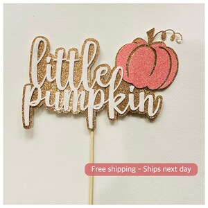 May include: Gold glitter cake topper with the words "little pumpkin" and a pink glitter pumpkin.
