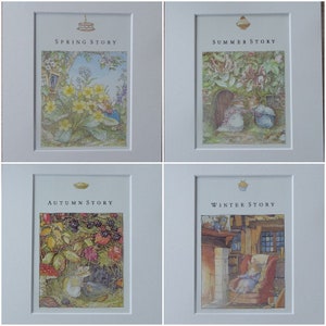 May include: Four framed illustrations depicting seasonal scenes. Each frame has a white mat and features a different image: Spring, Summer, Autumn, and Winter Story. The illustrations show charming animal characters in detailed, colorful settings, with text above each image.