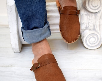 May include: A pair of brown leather slip-on shoes with a buckle strap. The shoes have a slightly pointed toe and a low heel.