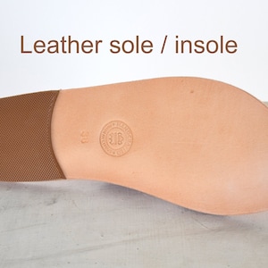May include: A close-up of a leather shoe sole and insole. The sole is light brown with a textured heel. The insole is a lighter shade of brown with a circular stamp and the number 38. The text "Leather sole / insole" is at the top.