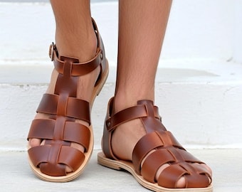 May include: A pair of brown leather gladiator sandals featuring a cage-style upper with wide straps, a closed heel, and an adjustable ankle strap with a small metal buckle. The sandals have a flat, light-coloured sole and a rounded toe design.