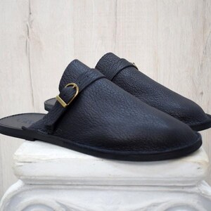 May include: A pair of black leather slip-on shoes with a buckle detail. The shoes have a flat sole and a pointed toe.