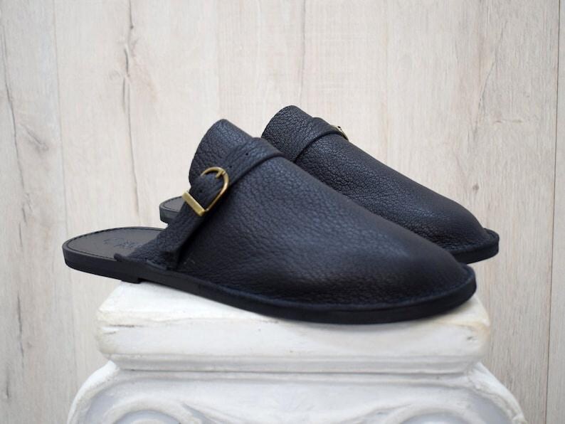 May include: A pair of black leather slip-on shoes with a buckle detail. The shoes have a flat sole and a pointed toe.