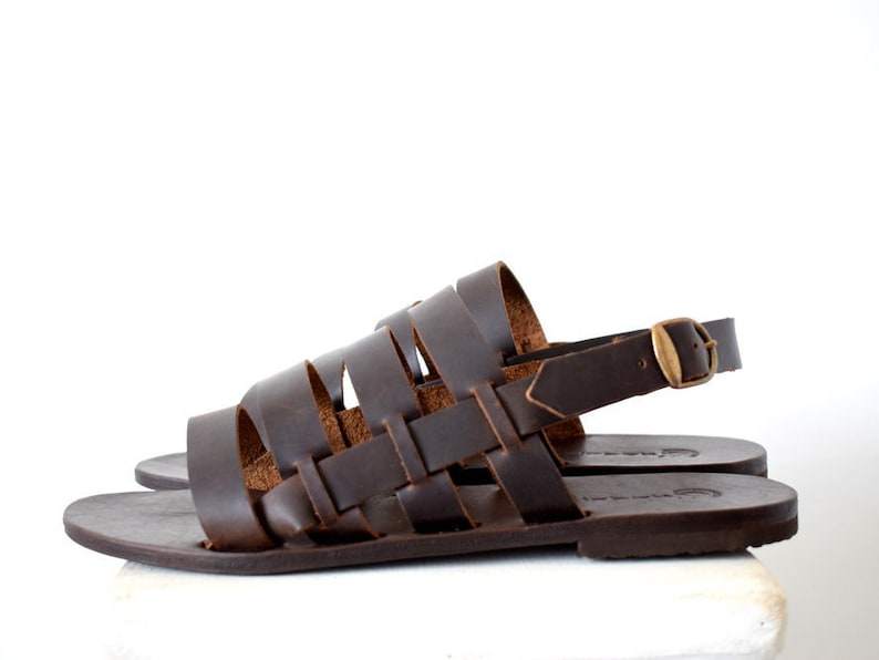 May include: Brown leather sandals with a woven strap design and an adjustable ankle strap with a gold buckle.