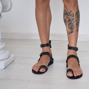 Pode incluir: Sand&aacute;lias de couro preto com uma al&ccedil;a para o dedo do p&eacute; e uma tira para o tornozelo. As sand&aacute;lias t&ecirc;m um design simples e s&atilde;o feitas de couro de alta qualidade.